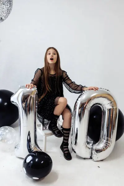 Küçük bir kız 10. yaş gününü kutluyor. Beyaz arka planda, siyah elbiseli, uzun düz saçlı bir kız. Parti, tatil. Yüksek kalite fotoğraf