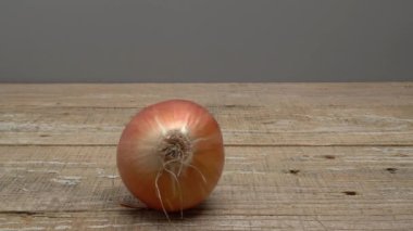 Gri arka planda ahşap bir zeminde soğanlar yuvarlanıyor. Video.