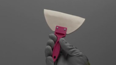 Beyaz kauçuk bir spatula gri arka planda bir el içinde döner. Video.