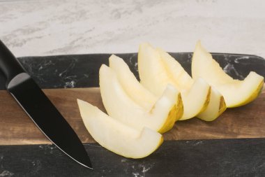 Kesme tahtasında siyah bir bıçakla taze dilimlenmiş armut, mutfak hazırlığı sergileniyor..