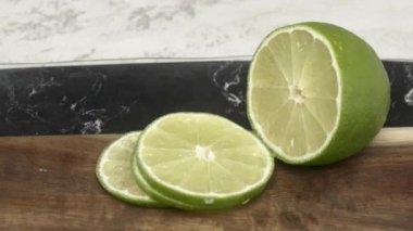 Video, tahta bir kesme tahtasının üzerinde dilimlenmiş limonları gösteriyor. Yeşil limon dilimleri, meyvelerin doğal güzelliğini vurgulayarak tahtayla tezat oluşturuyor.
