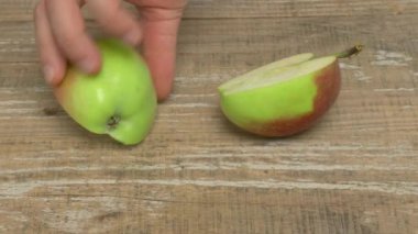İkiye bölünmüş canlı yeşil bir elma yanında bir bıçakla kırsal bir ahşap yüzeyde duruyor.