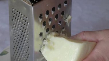 Bir el, güzel tasarlanmış bir çiçek tabağına yerleştirilmiş paslanmaz çelik rendeleyiciyi ustalıkla rendeliyor.