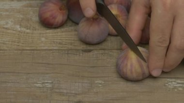 Kırsal bir ahşap yüzeyde olgun incir dilimleyen ellerin yakın çekimi, yemek pişirmek ve lezzetli tarifler için idealdir.