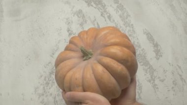 Gri desenli bir arka planın önünde olgun bir balkabağı tutan bir insan, sonbahar temalı içerik için mükemmeldir..