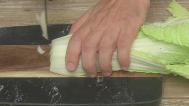 Salatalar ve çeşitli yemekler için ideal, kesme tahtasının üzerinde taze ve canlı marul doğrayan bir el.