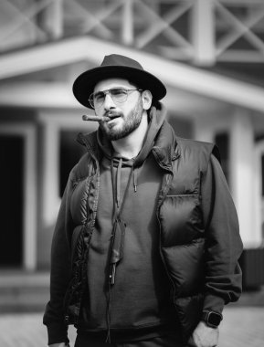 Sakallı, puro içen yakışıklı bir adamın portresi. Kovboy şapkalı genç beyaz adam evin önünde puro içiyor..