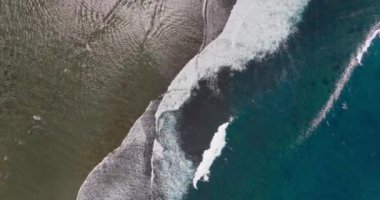 Güzel okyanus dalgaları üzerinde uçan bir dronun havadan görüntüsü ve yüksek açıyla kumlu bir sahile çarpan su..