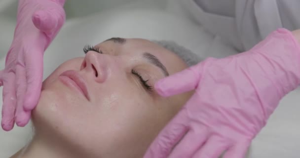 美容師は スパサロンで若い女性に栄養マスクを適用します 化粧品クリニックでトリートメントマスクで顔を楽しむ女性のクローズアップ 化粧品 スパについて — ストック動画