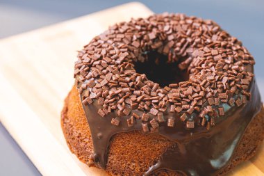 Chocolate cake with creamy chocolate sauce and decorated with chocolate sprinkles on a wooden board.