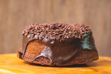 Chocolate cake with creamy chocolate sauce and decorated with chocolate sprinkles on a wooden board.