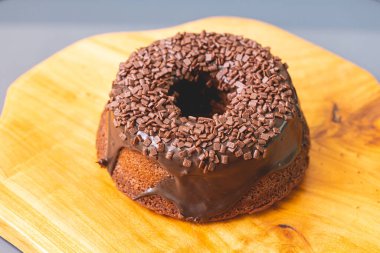 Chocolate cake with creamy chocolate sauce and decorated with chocolate sprinkles on a wooden board.