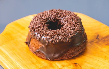 Chocolate cake with creamy chocolate sauce and decorated with chocolate sprinkles on a wooden board.