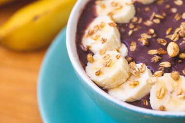Frozen acai with banana, condensed milk and granola served in a green bowl on a wooden board. Close-up photo. Brazilian food, dessert.