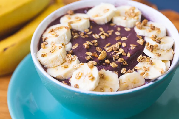Frozen acai with banana, condensed milk and granola served in a green bowl on a wooden board. Close-up photo. Brazilian food, dessert.