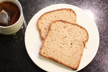 Arka planda bir fincan çay olan küçük beyaz bir tabakta iki dilim tam tahıllı ekmek. Makro fotoğrafçılık. Siyah granit arka plan.
