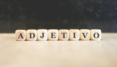 Portekizce ADJECTIVE kelimesi tahta küplere yazılmış. Siyah arkaplan. 