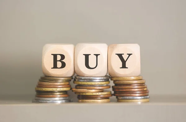 stock image Word BUY written on wooden cubes and coins on grey background. Studio photo.  