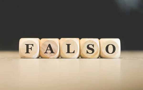 stock image The word FALSE in Brazilian Portuguese written on wooden cubes. Black background. 