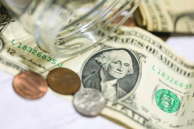 Makro fotoğrafçılıkta cam bir kavanozla ahşap bir masanın üzerinde Amerikan dolarları ve sikkeleri. Para tasarruf kavramı.
