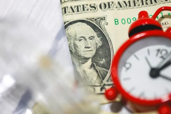 Stock image Dollar bills with glass jar on a wooden table with a red alarm clock in the composition. Money saving concept.