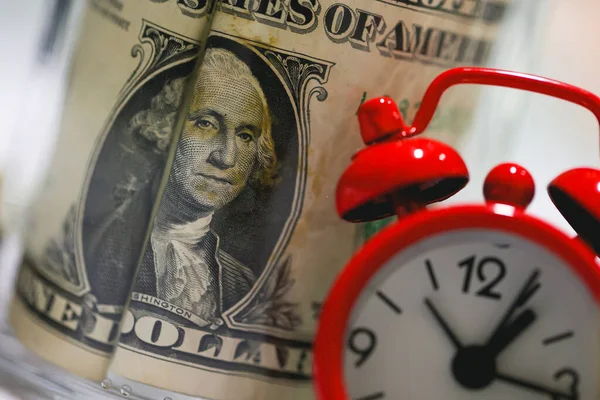 stock image Dollar bills with glass jar on a wooden table with a red alarm clock in the composition. Money saving concept.