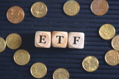 ETF Değiş tokuş Fonu kısaltması. Tahta küplere ve siyah arka planda bozuk paralara yazılmış..  