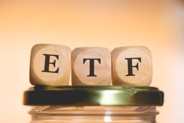 Tahta zarlara yazılan ETF kısaltması cam para tasarrufu kavanozunun üzerinde duruyordu. Stüdyo fotoğrafı.