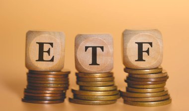 Tahta zarlara yazılan ETF kısaltması bozuk para yığınlarının üzerinde duruyor. Stüdyo fotoğrafı.