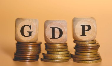 GSYİH kısaltması, bozuk para yığınlarının üzerinde duran tahta zarlar üzerine yazılmış. Stüdyo fotoğrafı.