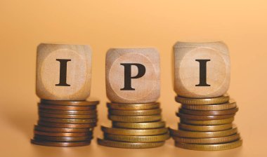 Tahta zarların üzerine yazılan IPI kısaltması bozuk para yığınlarının üzerinde duruyor. Stüdyo fotoğrafı.