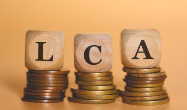 LCA kısaltması, bozuk para yığınlarının üzerinde duran tahta zarlar üzerine yazılmış. Stüdyo fotoğrafı.