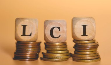 LCI kısaltması, bozuk para yığınlarının üzerinde duran tahta zarlara yazılmış. Stüdyo fotoğrafı.