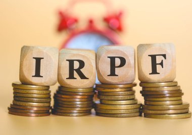 Acronym IRPF written on wooden cubes and piles of coins. Studio photo. clipart