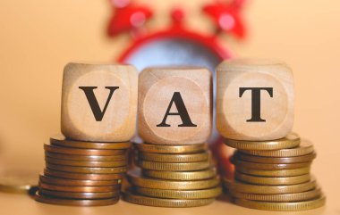 Acronym VAT for Value-Added Tax written on wooden cubes and piles of coins. Studio photo. clipart