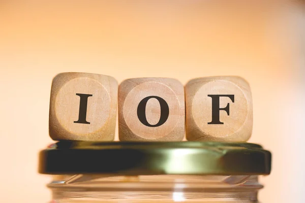 stock image The abbreviation IOF written on wooden dice lying on top of a glass money-saving jar. Studio photo.