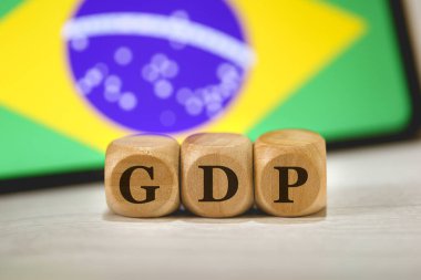 Ahşap küplere yazılmış gayri safi yurtiçi hasılanın kısaltması. Kompozisyonunda Brezilya bayrağı olan bir cep telefonu..