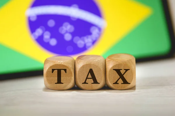 在木制立方体上写的单词Tax 在作文中 一个屏幕上有巴西国旗的手机 — 图库照片