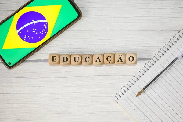 木製のテーブルの上に木製のキューブに書かれたポルトガル語でのテキスト教育 組成物中のブラジルの旗を持つノートブック 携帯電話 — ストック写真