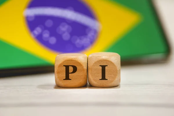 木製の立方体に書かれた頭字語のPi 構成で画面上のブラジルの旗を持つ携帯電話 — ストック写真