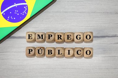 Brezilya Portekizcesinde tahtadan küplere yazılmış PUBLIC EMPLOYMENT metni. Kompozisyonda ekranda Brezilya bayrağı olan bir cep telefonu gösteriliyor.