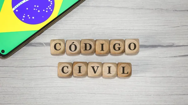 The text CIVIL CODE in Brazilian Portuguese written on wooden cubes. A cell phone with the Brazilian flag being shown on the screen in the composition.