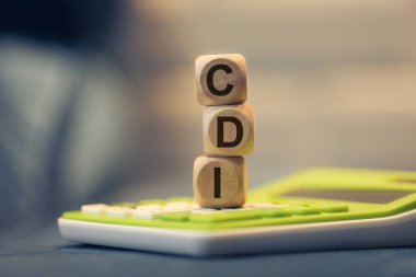 Brezilya Portekizcesi tahtadan küplere yazılmış Bankalar Arası Mevduat Sertifikası kısaltması CDI. Kompozisyonda bir hesap makinesi. 