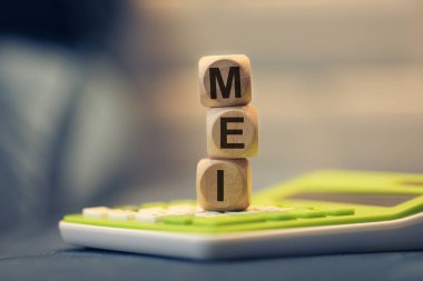 Bireysel Mikrogirişimciler için kısaltma MEI. Tahta küplere yazılmış. Kompozisyonda bir hesap makinesi. 