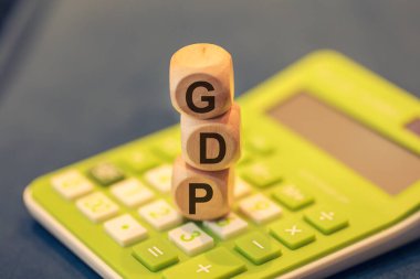 Ahşap küplere yazılmış gayri safi yurtiçi hasılanın kısaltması. Kompozisyonda bir hesap makinesi. 