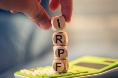Close-up view of man forming acronym IRPF with wooden cubes. A calculator in the composition.  clipart