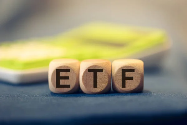 ETF acronym for Exchange Traded Fund written on wooden cubes. A calculator in the composition.