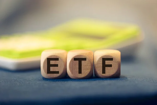 ETF acronym for Exchange Traded Fund written on wooden cubes. A calculator in the composition.