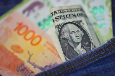 Argentine peso banknotes and United States dollar bills in a jeans pocket in macro photo. clipart