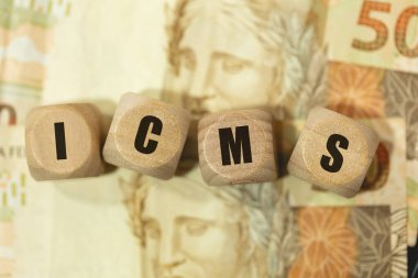 The abbreviation ICMS for Tax on Circulation of Goods and Services written on wooden dice in Brazilian Portuguese. 50 Reais notes in the composition. clipart